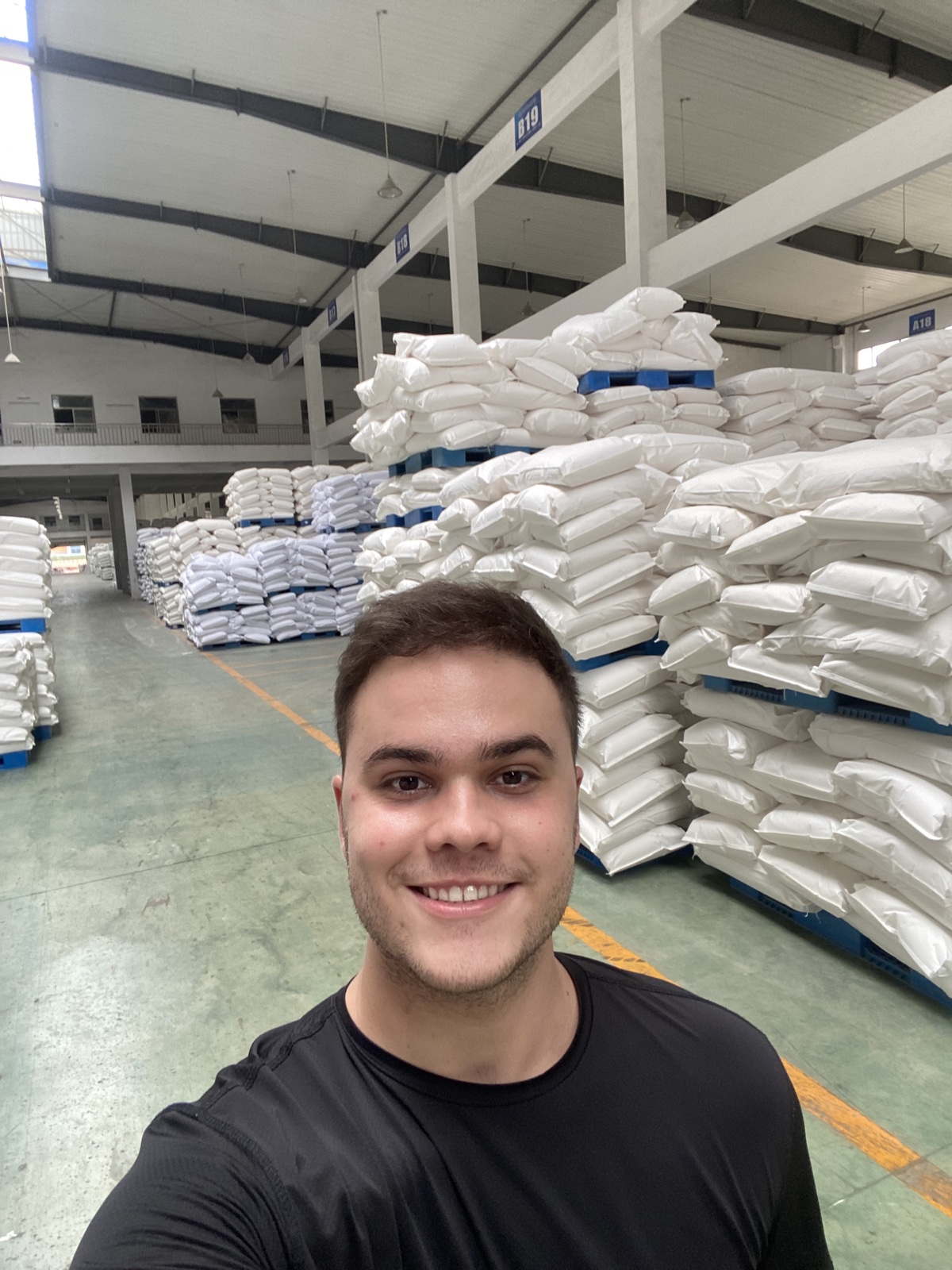 Henrique em um armazém com pilhas de sacos ao fundo